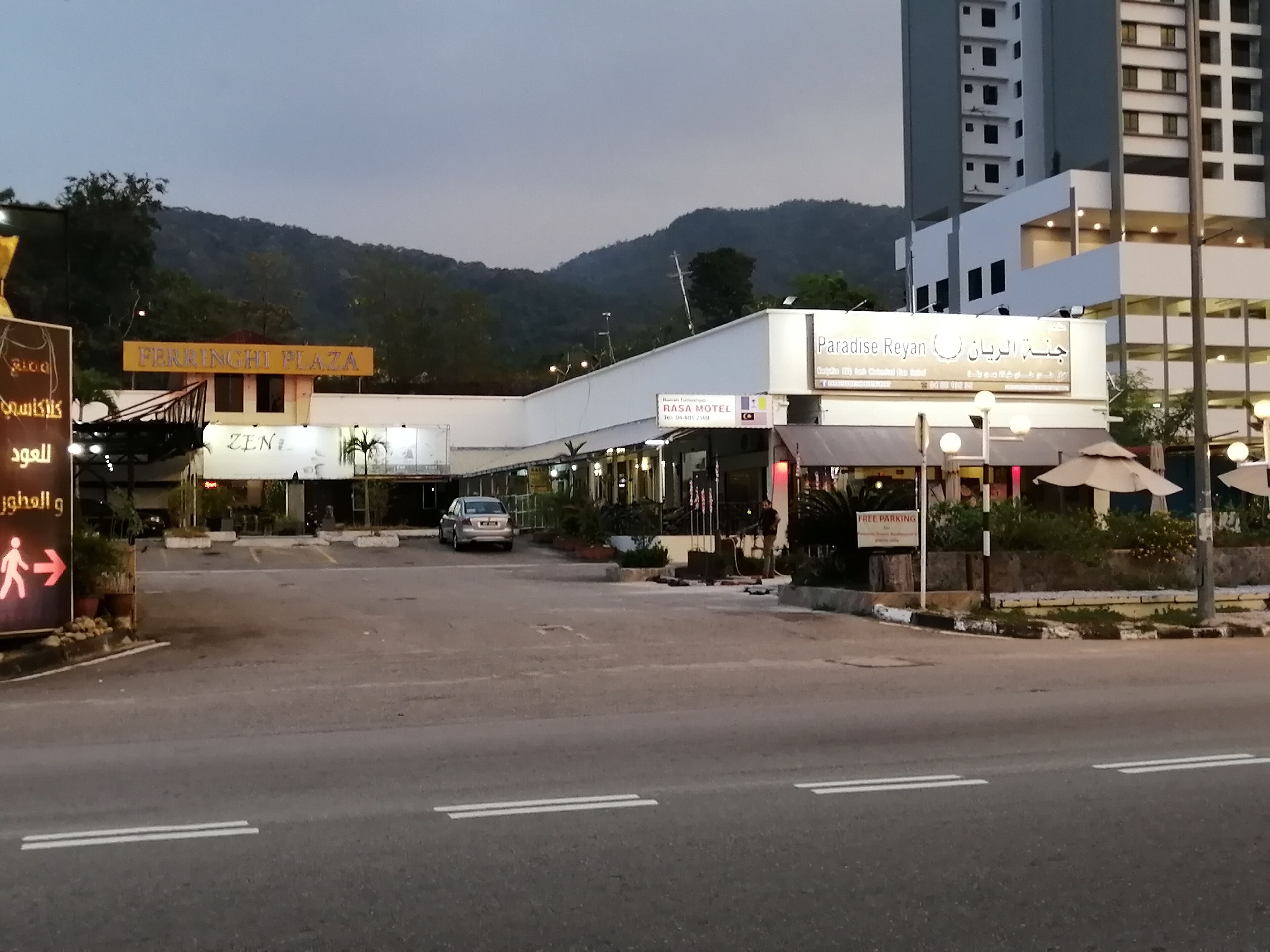 Une vue de rue montrant une zone de stationnement devant un immeuble sur lequel on peut lire l’inscription « Paradise Reyan ».