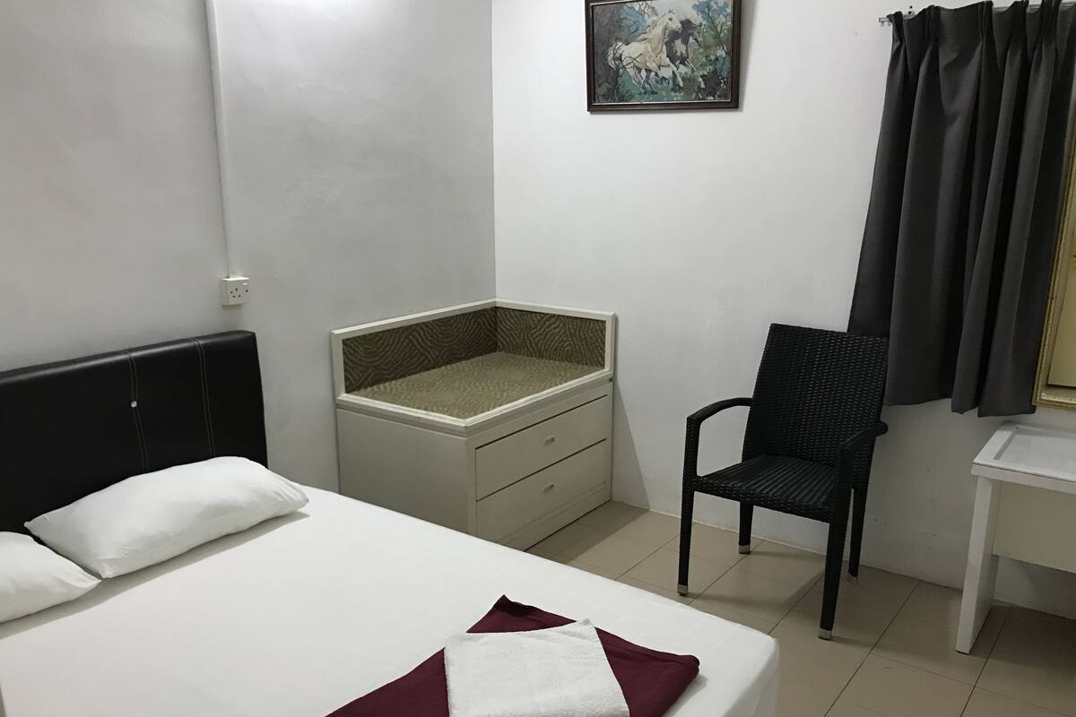 A hotel room with a bed, a nightstand, a chair, a desk, and a painting on the wall.