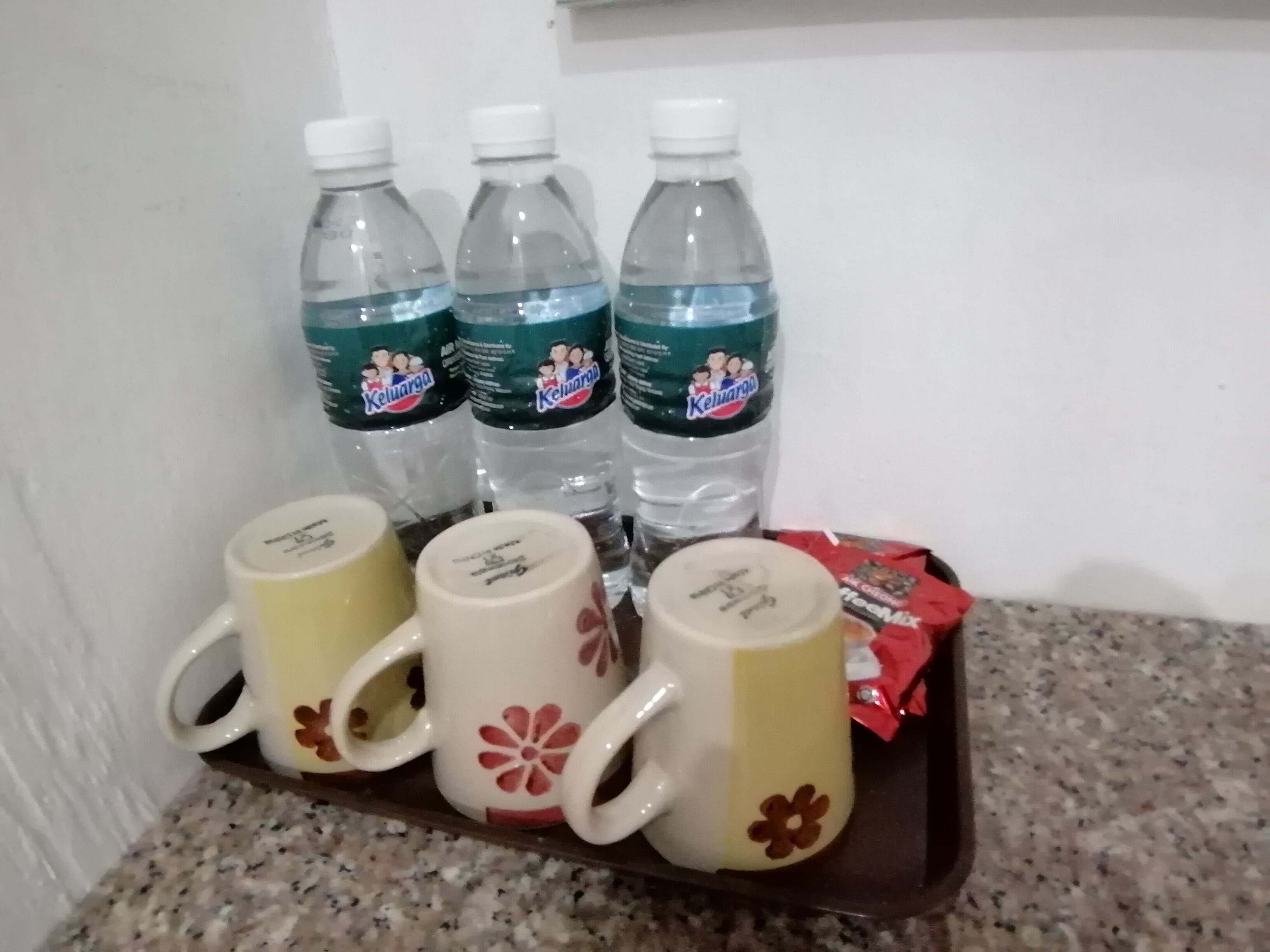 A tray with three water bottles and three mugs on a granite countertop.