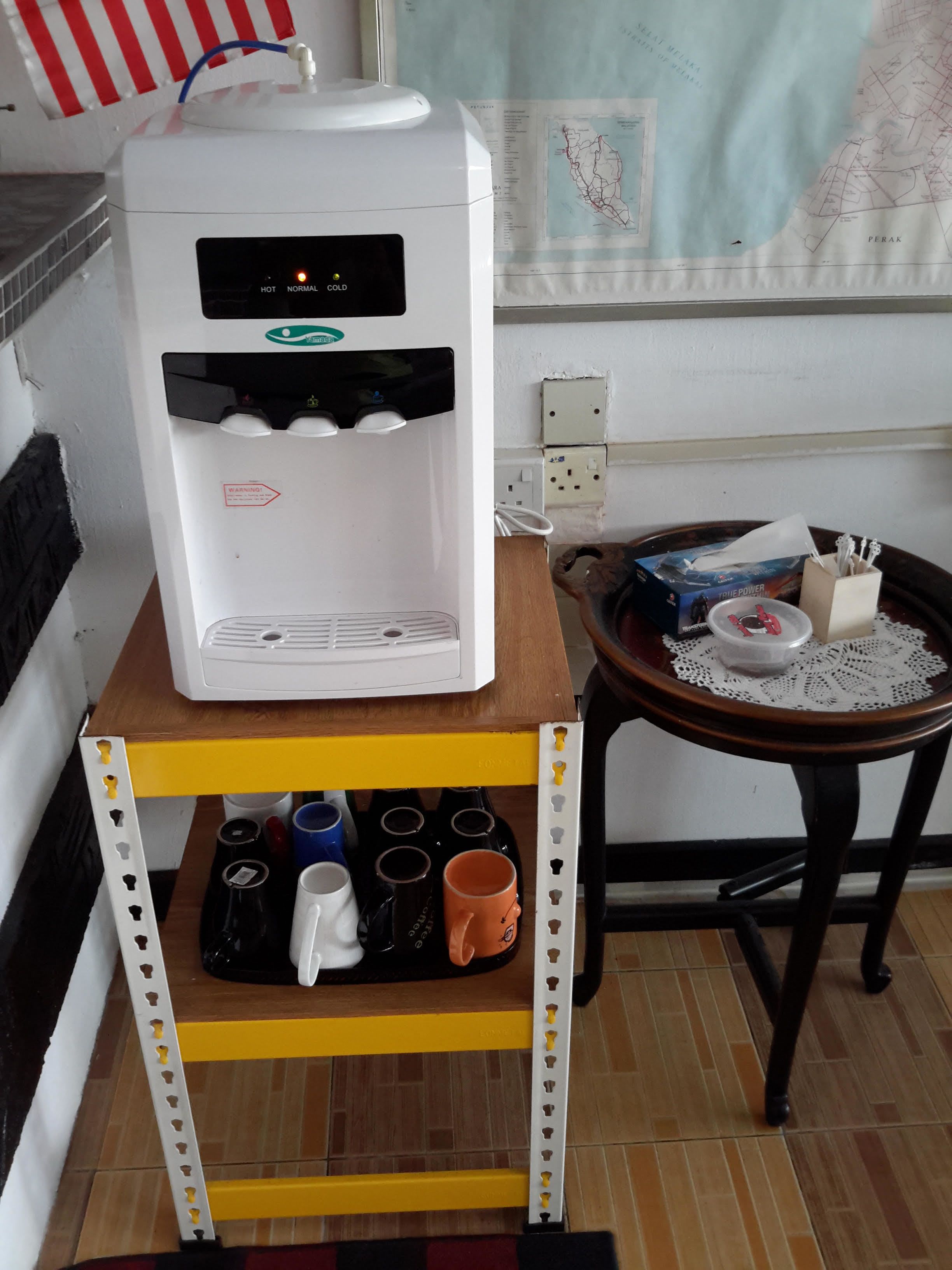A water dispenser on a yellow shelf, a small table with a box and utensils, and a map on the wall.