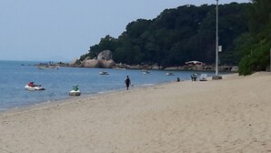 A beach with boats, a person walking, and a rocky hill in the background. - Rasa Motel (George Town)