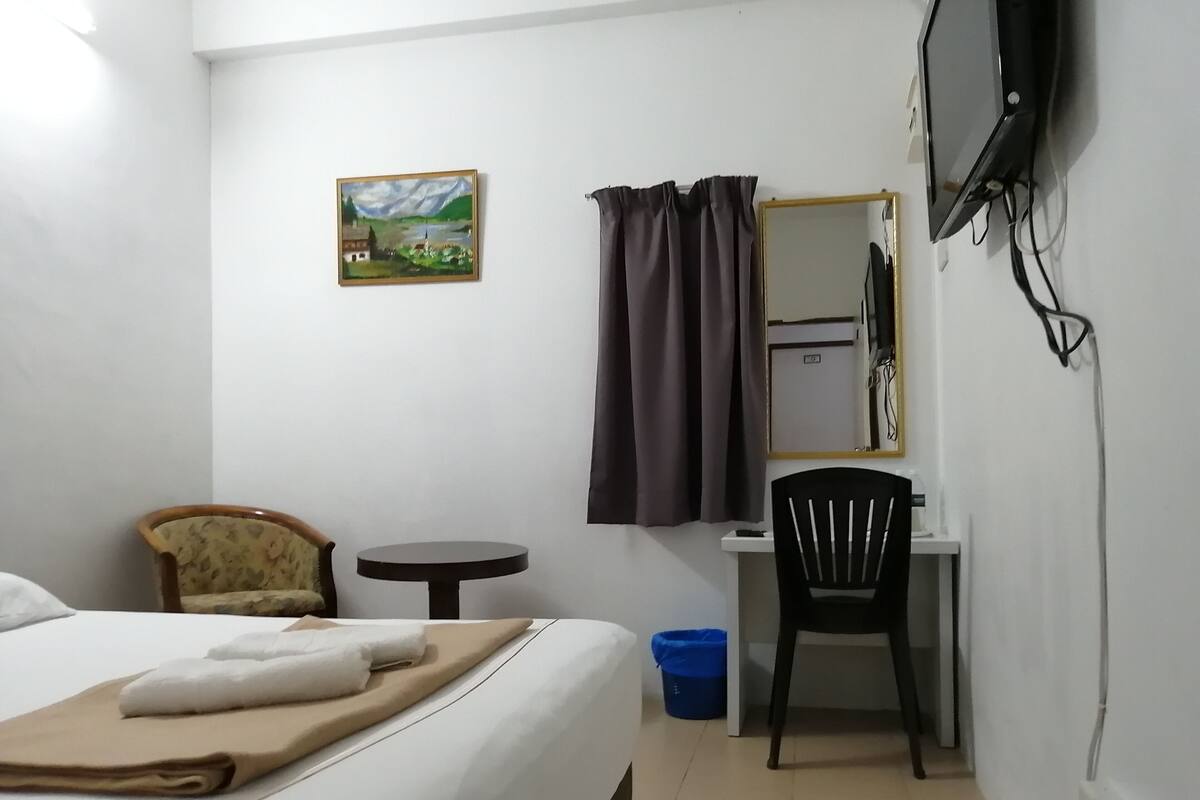 A hotel room with a bed, a desk, a chair, a television, a painting, and a curtain.