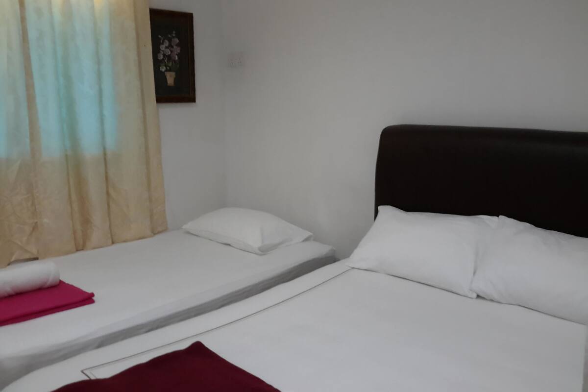 A room with two beds, a window with curtains, a wall-mounted picture, and a white wall.