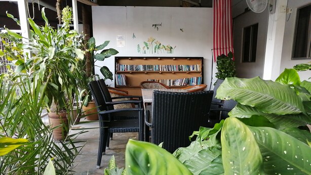 A cozy reading nook with wicker furniture, a bookshelf, and lush green plants. - Rasa Motel (George Town)