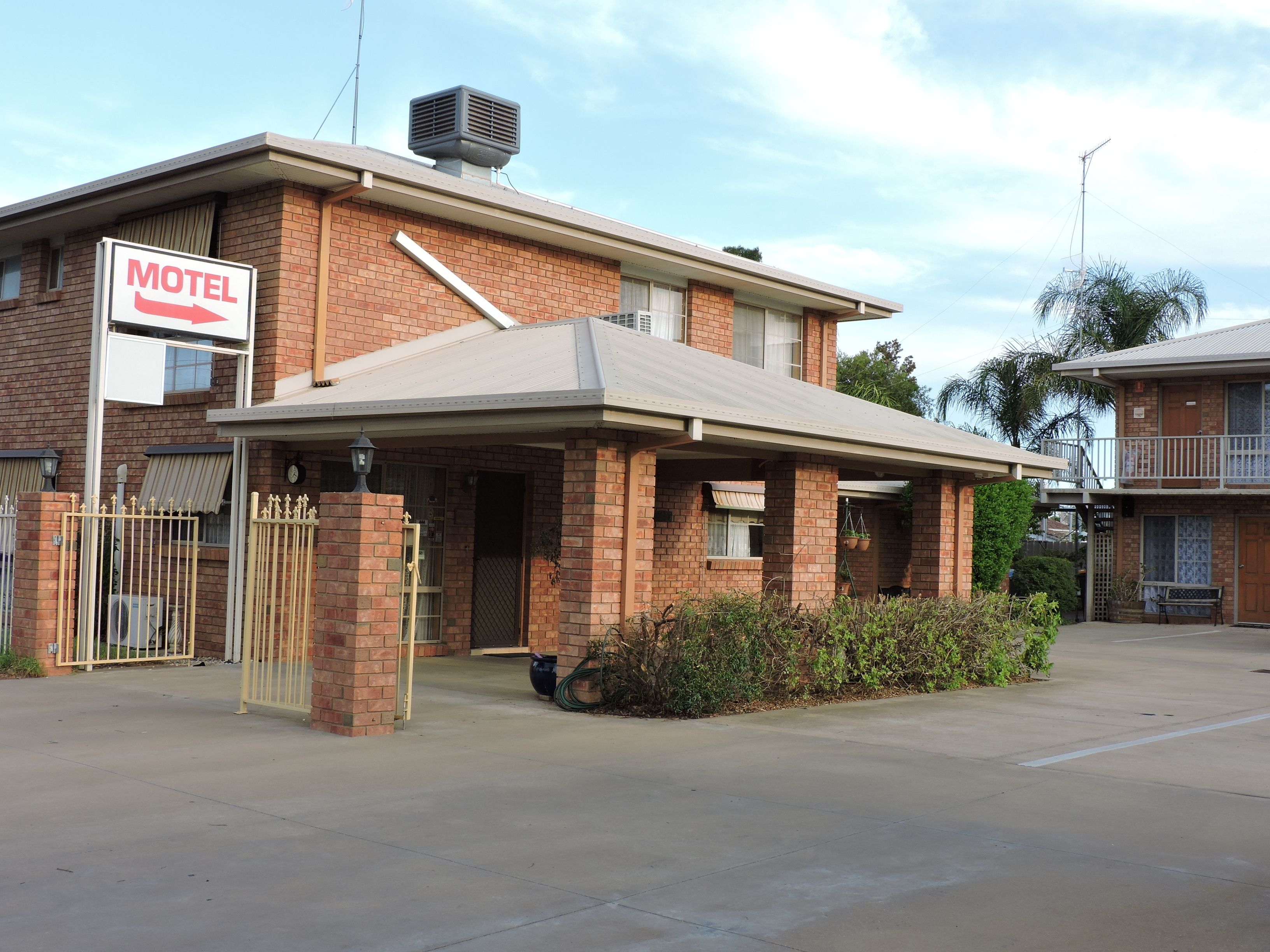 Un motel de dos pisos con fachada de ladrillo, área de estacionamiento techada y un letrero que indica su función.