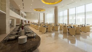 Un amplio hall de hotel con una larga mesa de buffet, varias zonas de estar y grandes ventanales que aportan luz natural.