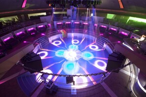 A circular atrium with a central light fixture, seating areas, and a stage with speakers. - United-21 The Grand (Pune)