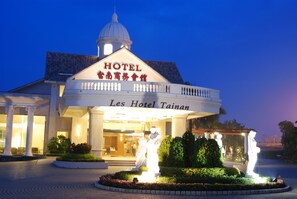 Un hotel con cúpula y columnas, llamado "Les Hotel Tainan", que presenta una entrada bien iluminada y una estatua en el jardín.