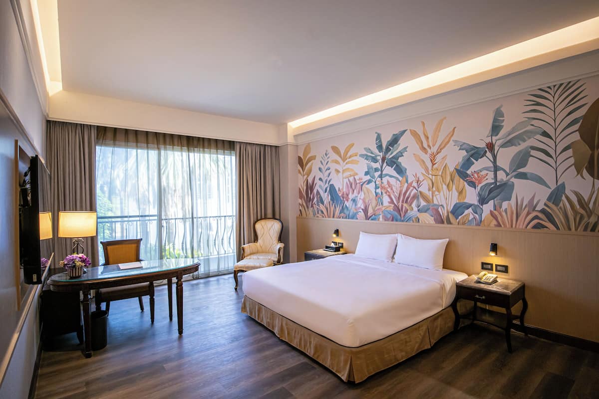 A hotel room with a large bed, a desk with a lamp, a chair, and a nightstand with a phone.