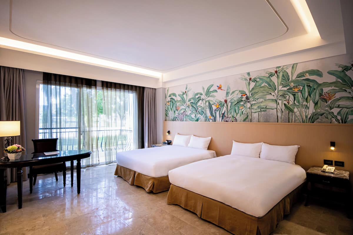 A hotel room with two beds, a desk with a chair, a piano, and a large botanical mural on the wall.