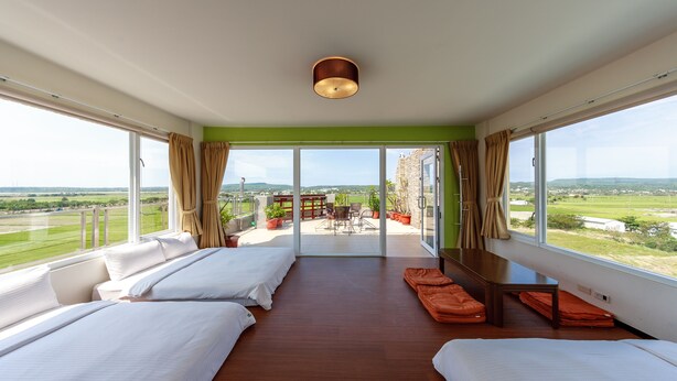 A spacious bedroom with two beds, a balcony with a table and chairs, and a view of the countryside. - Kenting Green Yard B&B (Hengchun)