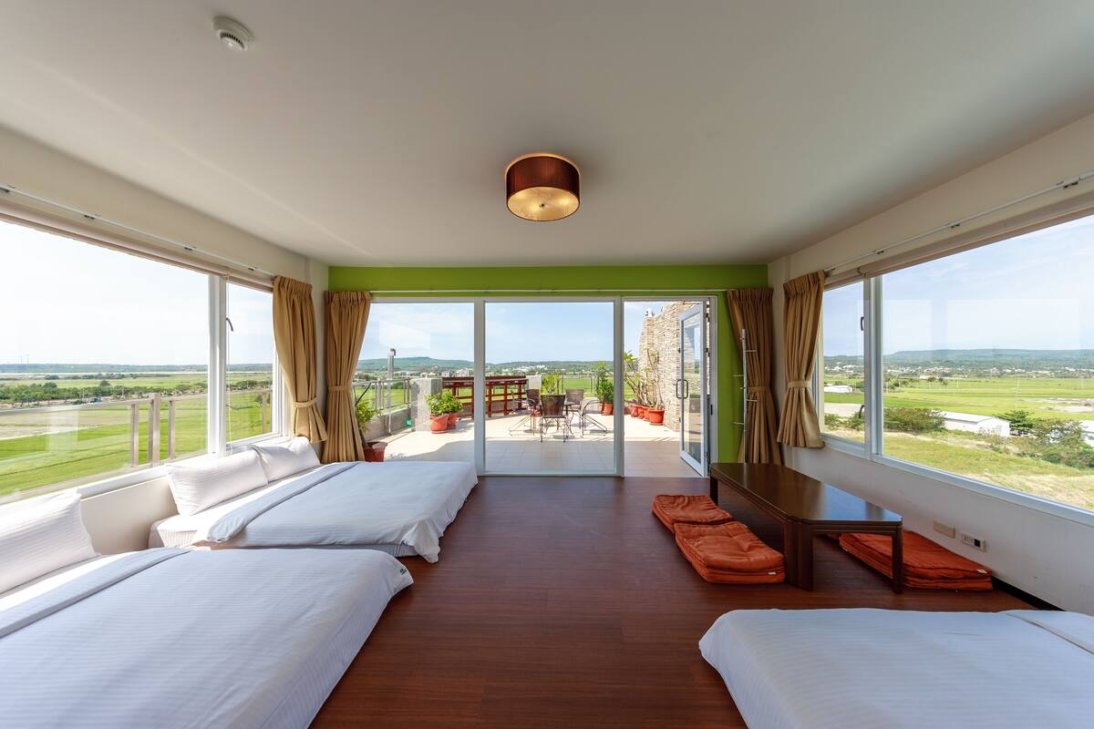 A spacious bedroom with two beds, a balcony with a table and chairs, and a view of the countryside.