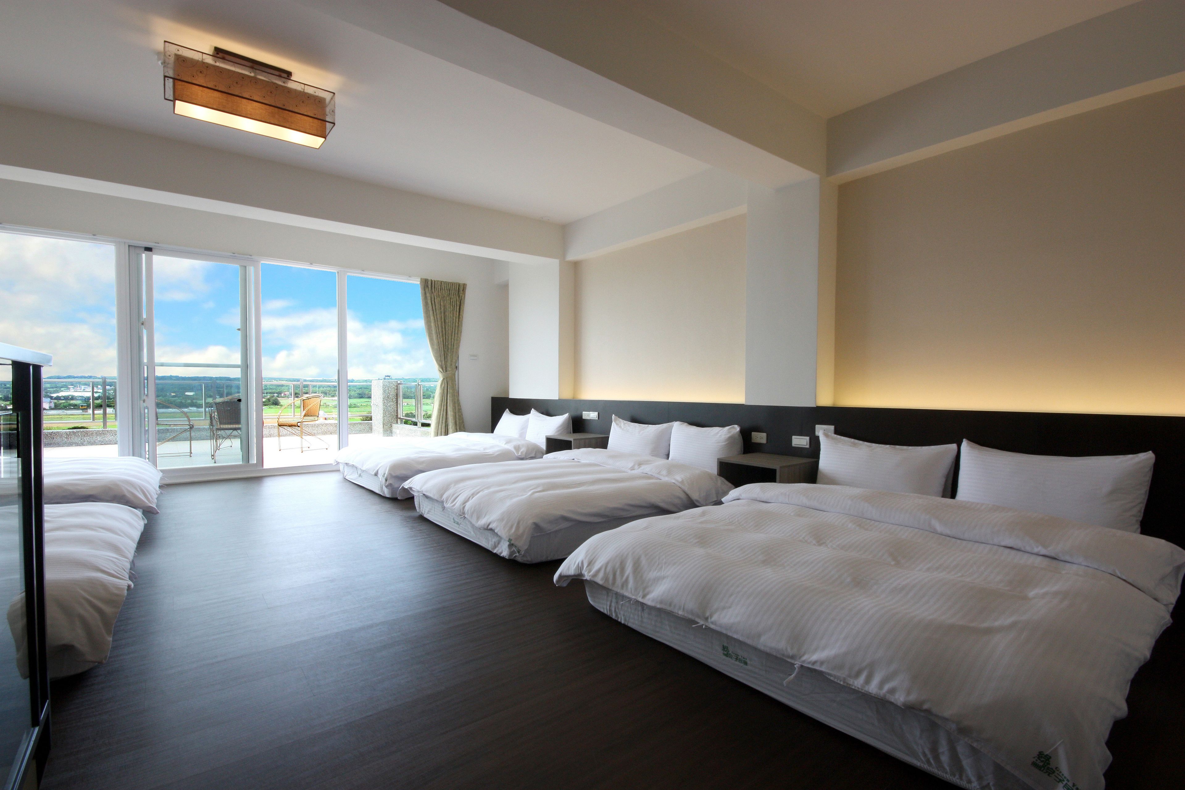 A hotel room with a large bed, a TV, and a balcony with a city view.