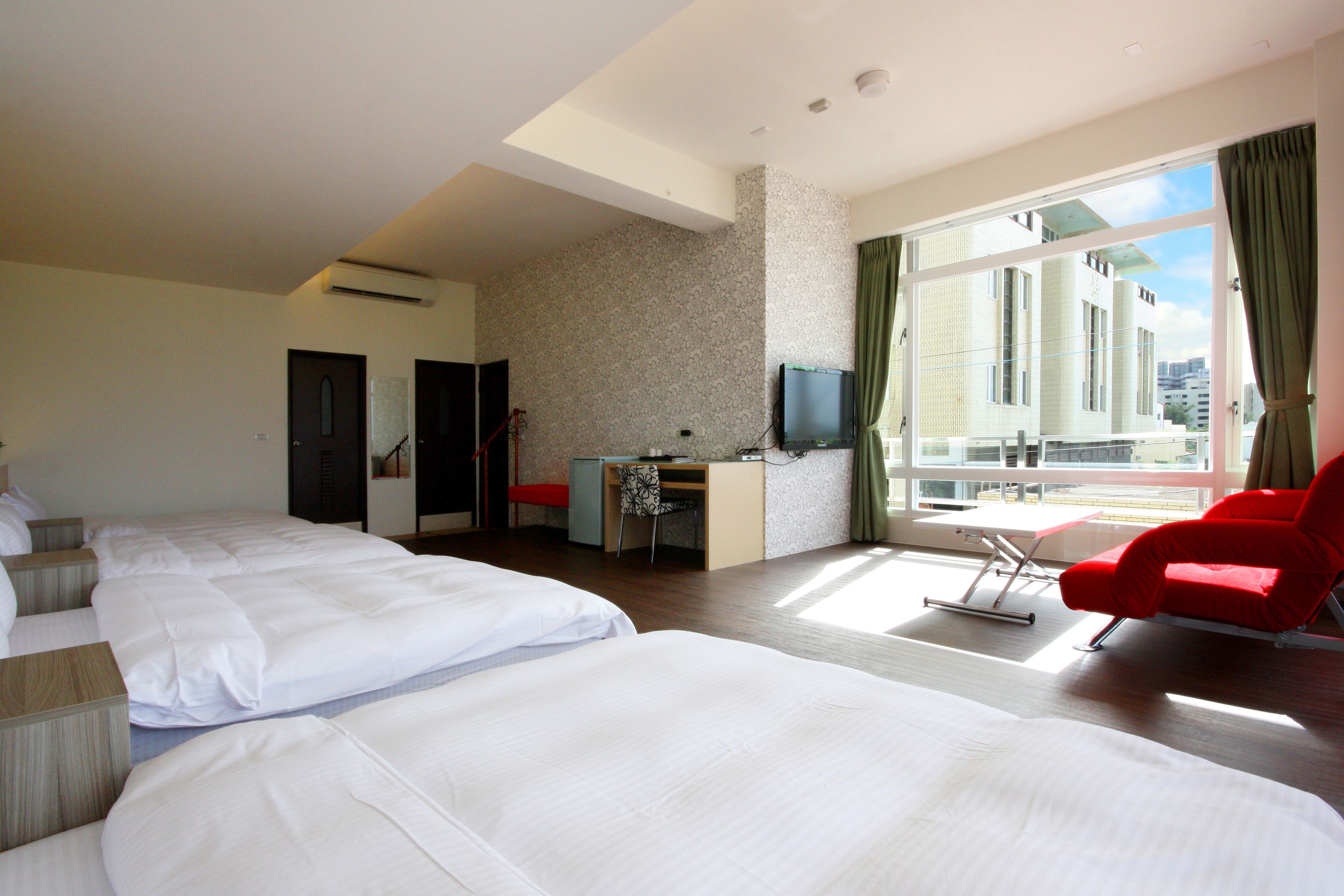 A hotel room with two beds, a desk, a TV, and a red chair.
