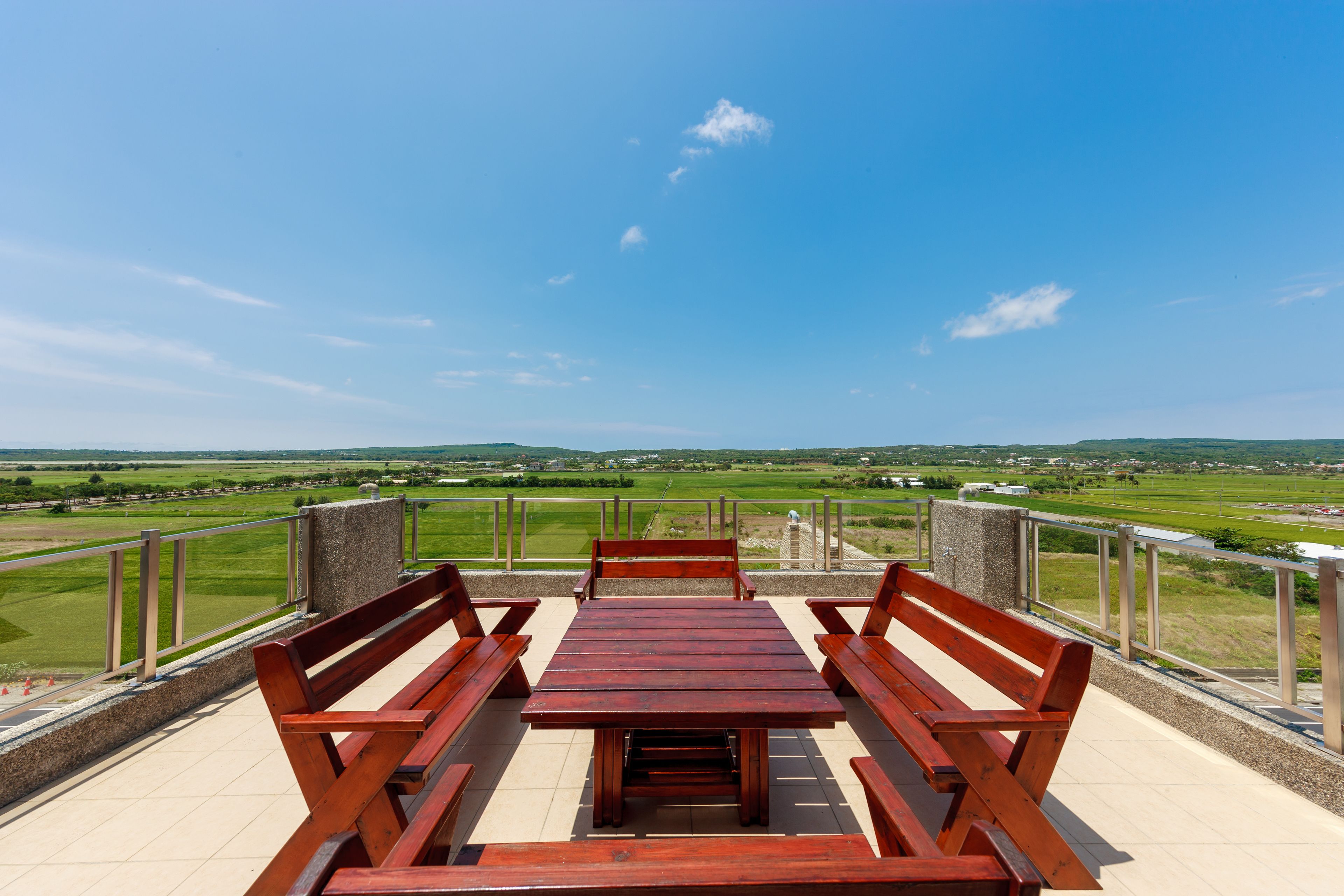 A terrace with a wooden table and benches, offering a view of a green landscape.