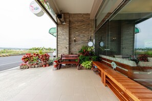 A cafe with outdoor seating, a stone wall, and a view of the road. - Kenting Green Yard B&B (Hengchun)