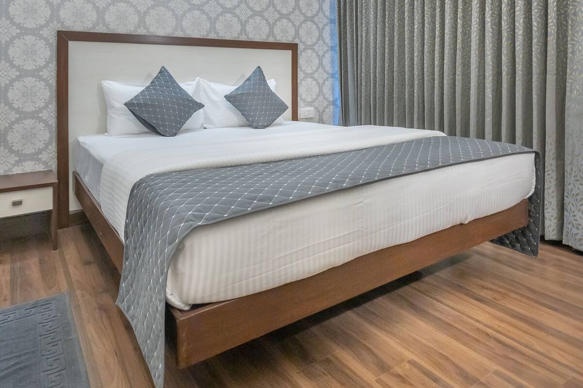 Un dormitorio ordenado con una cama grande, una mesita de noche, un equipo de aire acondicionado y un candelabro colgante.