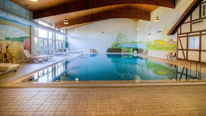 An indoor swimming pool with lounge chairs, a mural, and wooden beams on the ceiling.