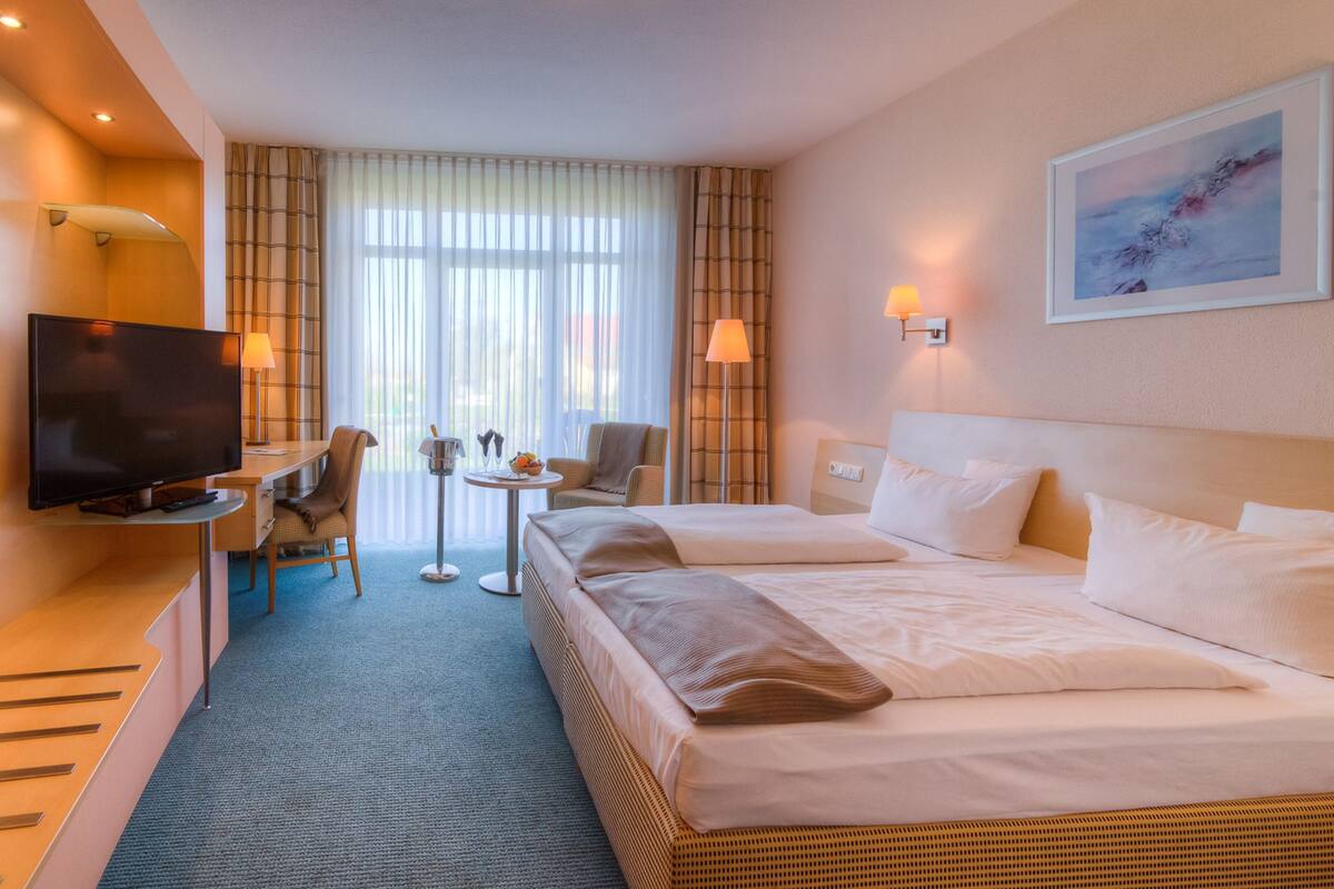 A hotel room with a large bed, a TV, a desk, and a chair.