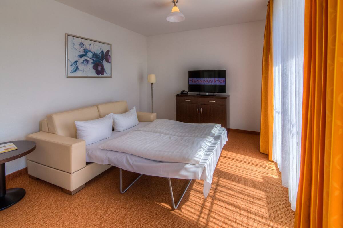 A hotel room with a bed, a sofa, a television, and a painting on the wall.