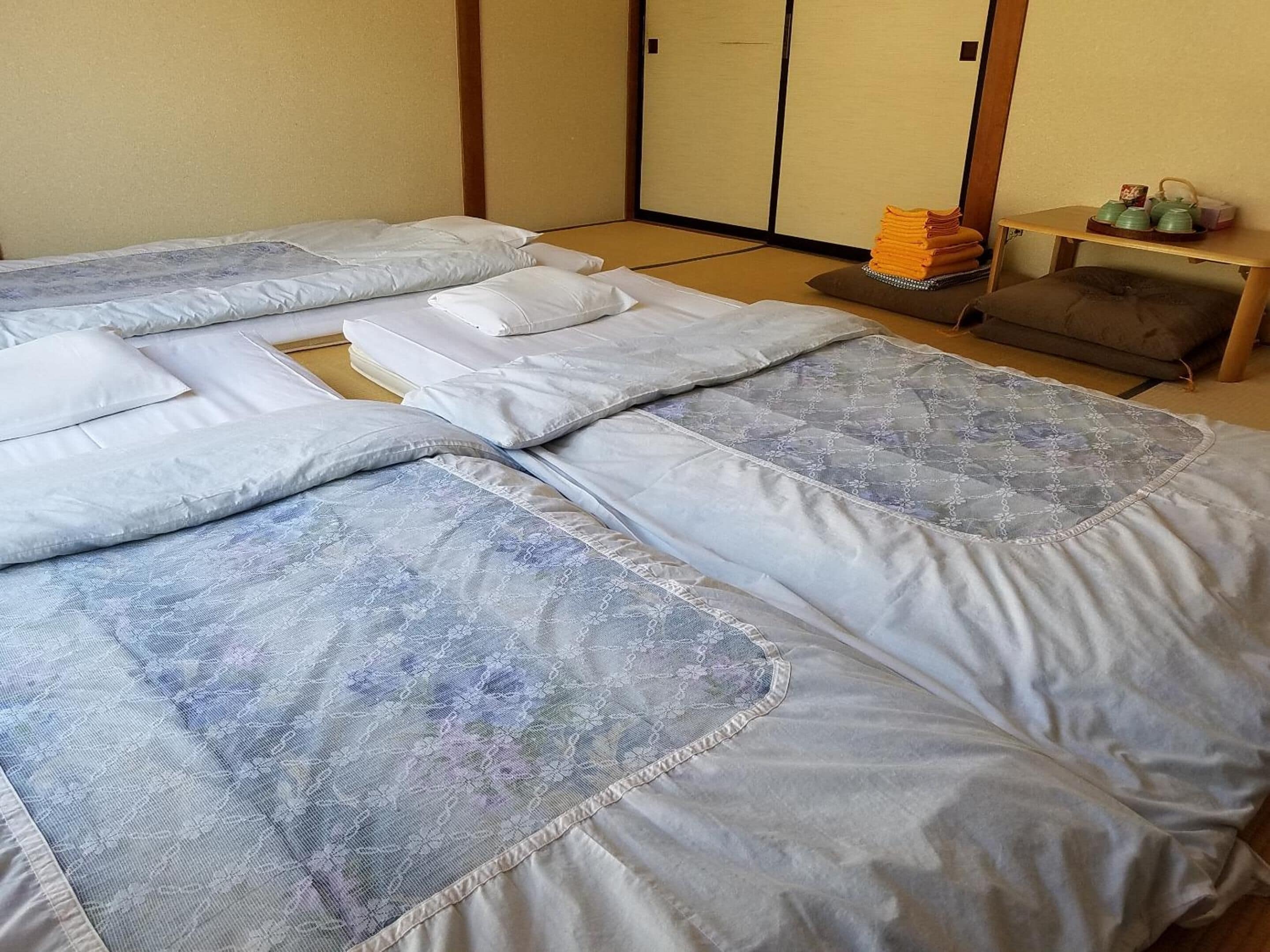 A hotel room with a bed, pillows, a small table with a tray of towels, and a futon.