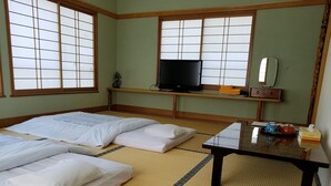 Een traditionele Japanse kamer met tatami matten, twee bedden, een televisie, een klein tafeltje met theeservies en een spiegel.