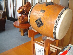 Un tambour japonais traditionnel, doté d’une caisse en bois et d’éléments décoratifs en métal, est exposé sur un support en bois, avec une étiquette placée à l’avant.