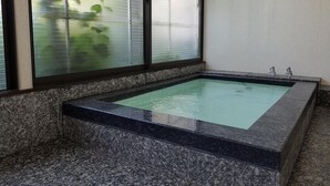 Een rechthoekig whirlpool met een granieten rand, geplaatst tegen een muur met glasgeëtste ramen.
