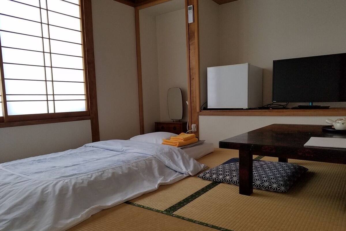 Ein Zimmer mit einem Bett, einem Fernseher, einem Schreibtisch und einem Fenster mit Jalousien.