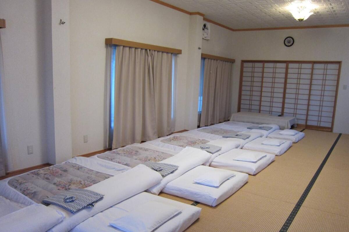 Ein Zimmer mit mehreren nebeneinanderliegenden Betten, jeweils mit Kopfkissen und Decke.