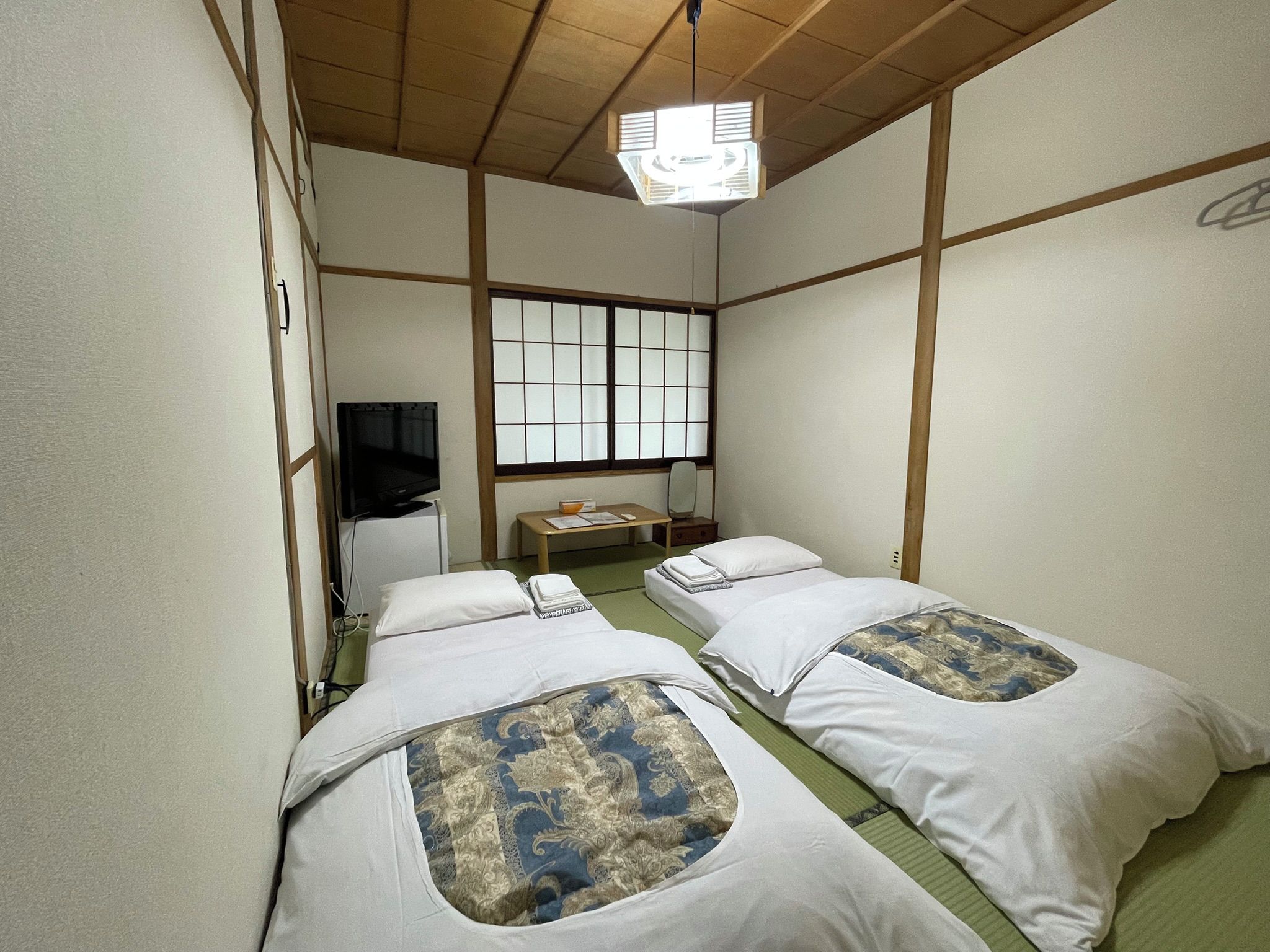 Quarto japonês tradicional com tatames, duas camas individuais com roupa de cama estampada, uma televisão e uma janela com vista.