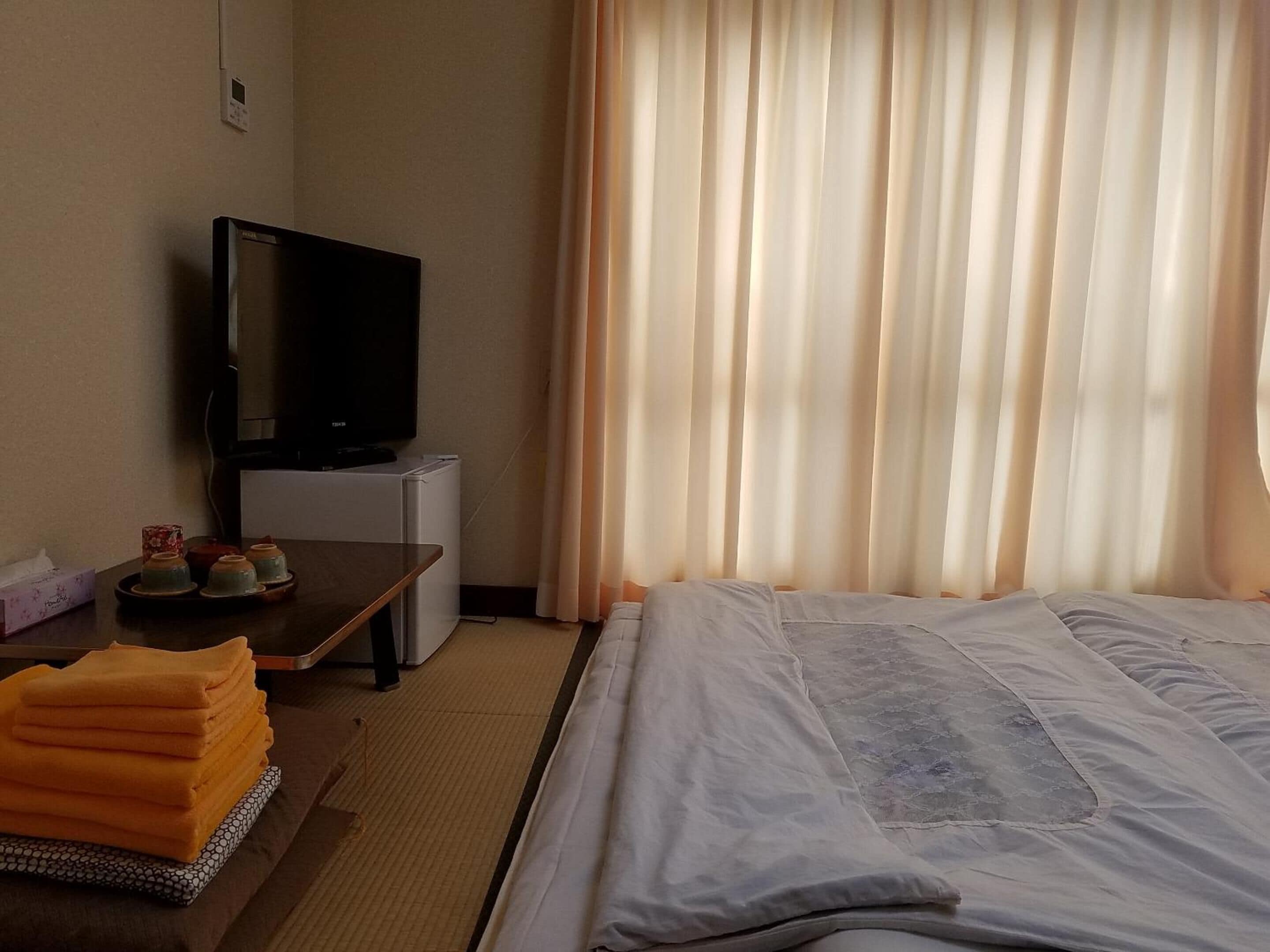 A hotel room with a bed, a desk with a TV, a small refrigerator, and a window with curtains.