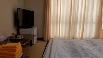 A hotel room with a bed, a desk with a TV, a small refrigerator, and a window with curtains.