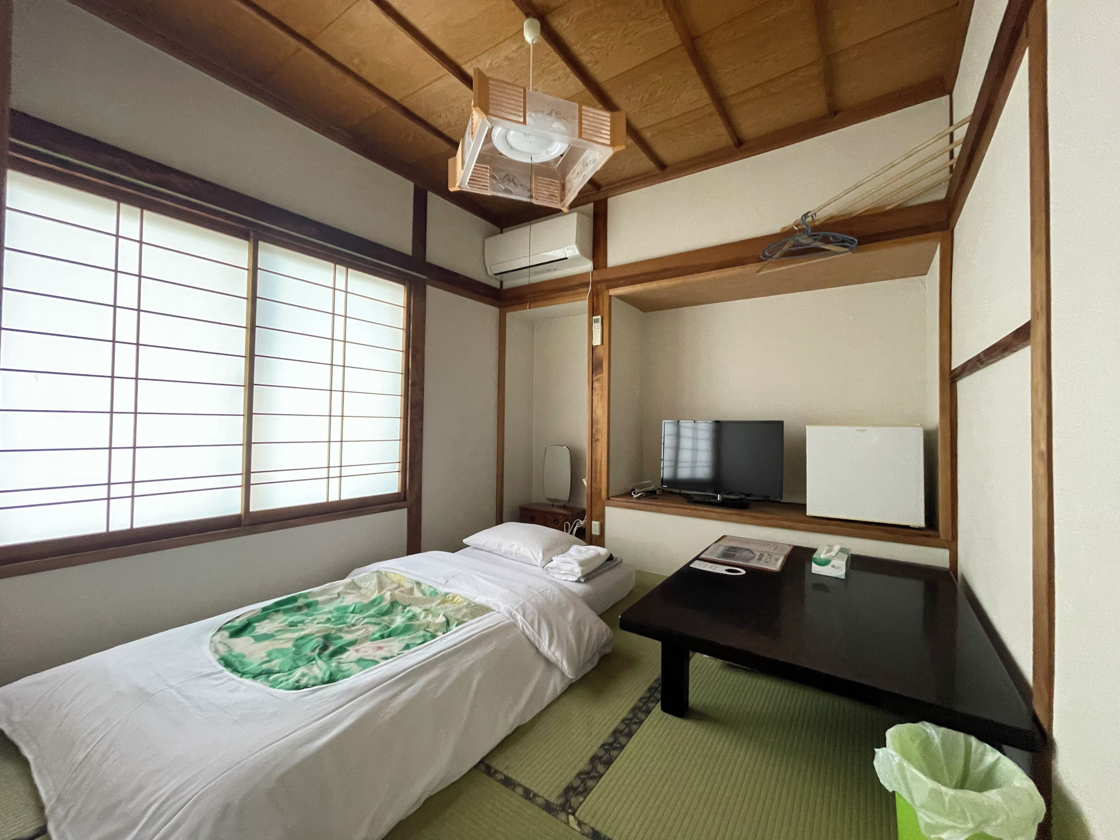 Una habitación tradicional japonesa con suelo de tatami, futón, televisor y techo de madera.