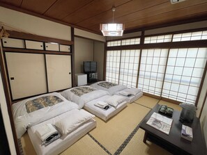 A traditional Japanese-style room with tatami flooring, two beds with pillows, a television, and a view through shoji screens. - Ryokan Matsukaze (Matsumoto)