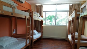 A dormitory room with bunk beds, wooden floors, a window with curtains, and a visible electrical outlet. - Backpackers@SG - Hostel (Singapore)