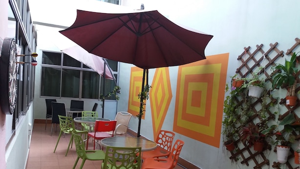 A small outdoor seating area with a table and chairs, a large umbrella, and a wall decorated with geometric patterns and potted plants. - Backpackers@SG - Hostel (Singapore)