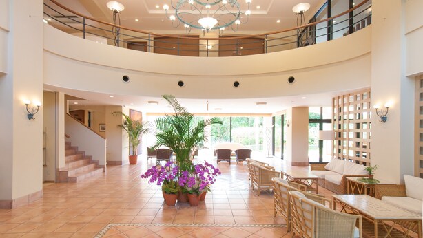 Un hall d’entrée spacieux avec un escalier central, des plantes en pot et des coins salon.