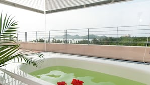 Une salle de bain moderne avec une baignoire, une vue sur un plan d’eau et un balcon doté d’une balustrade.