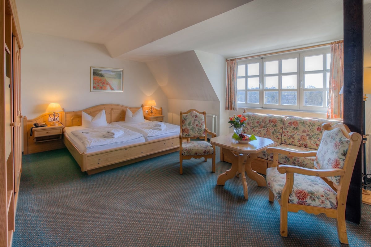 A bedroom with a bed, two chairs, a table, and a window.