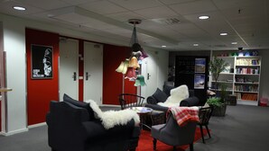 A modern lounge area with a black sofa, a grey armchair, a small round table, and a bookshelf filled with books. - STF Gärdet Hotel & Hostel (Stockholm)