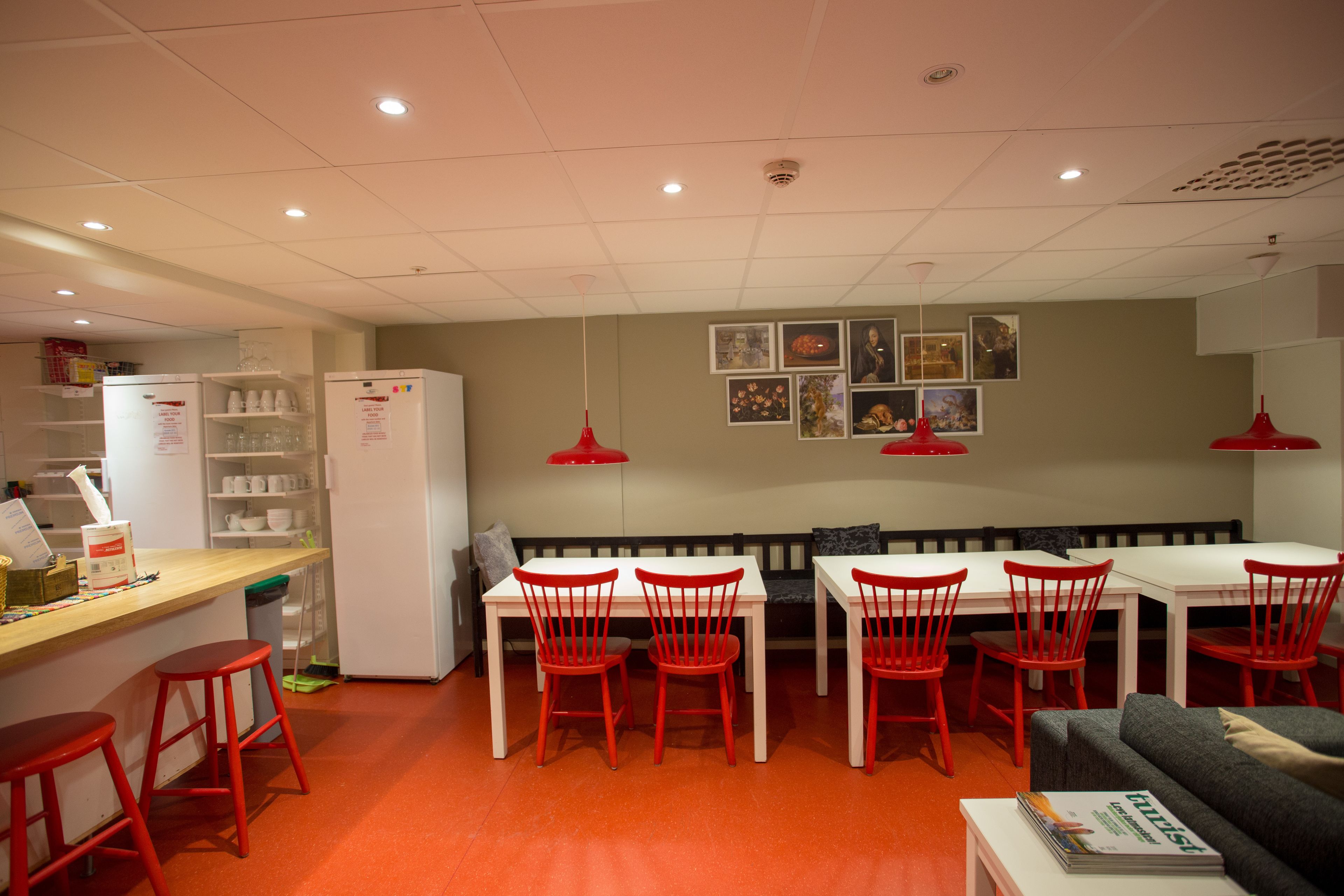 A compact kitchen with a dining area, featuring a white refrigerator, red chairs, and a white table.