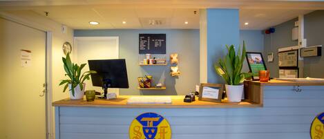 A reception desk with a computer monitor, a menu board, and potted plants.