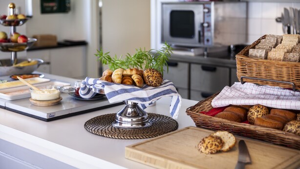 A kitchen counter with various food items, including bread, pastries, and a bowl of fruit. - STF Gärdet Hotel & Hostel (Stockholm)