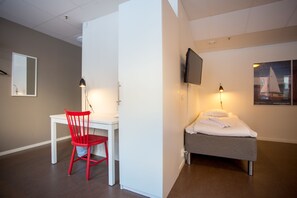 A hotel room with a white desk, a red chair, a bed with a TV mounted above it, and a framed picture on the wall. - STF Gärdet Hotel & Hostel (Stockholm)