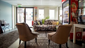 A lobby with a sofa, two armchairs, a Coca-Cola refrigerator, and a patterned rug with city names. - STF Gärdet Hotel & Hostel (Stockholm)