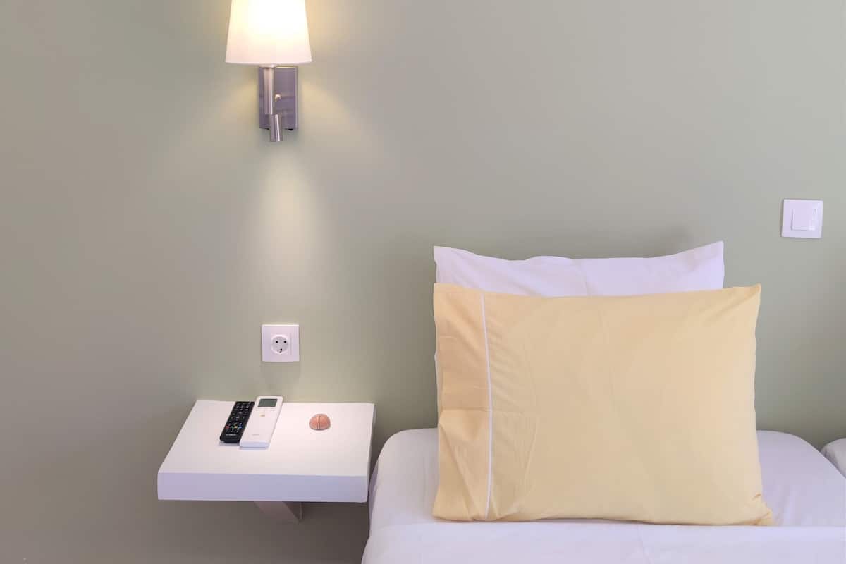 A hotel room with a bed, a nightstand with a lamp, and a power outlet.