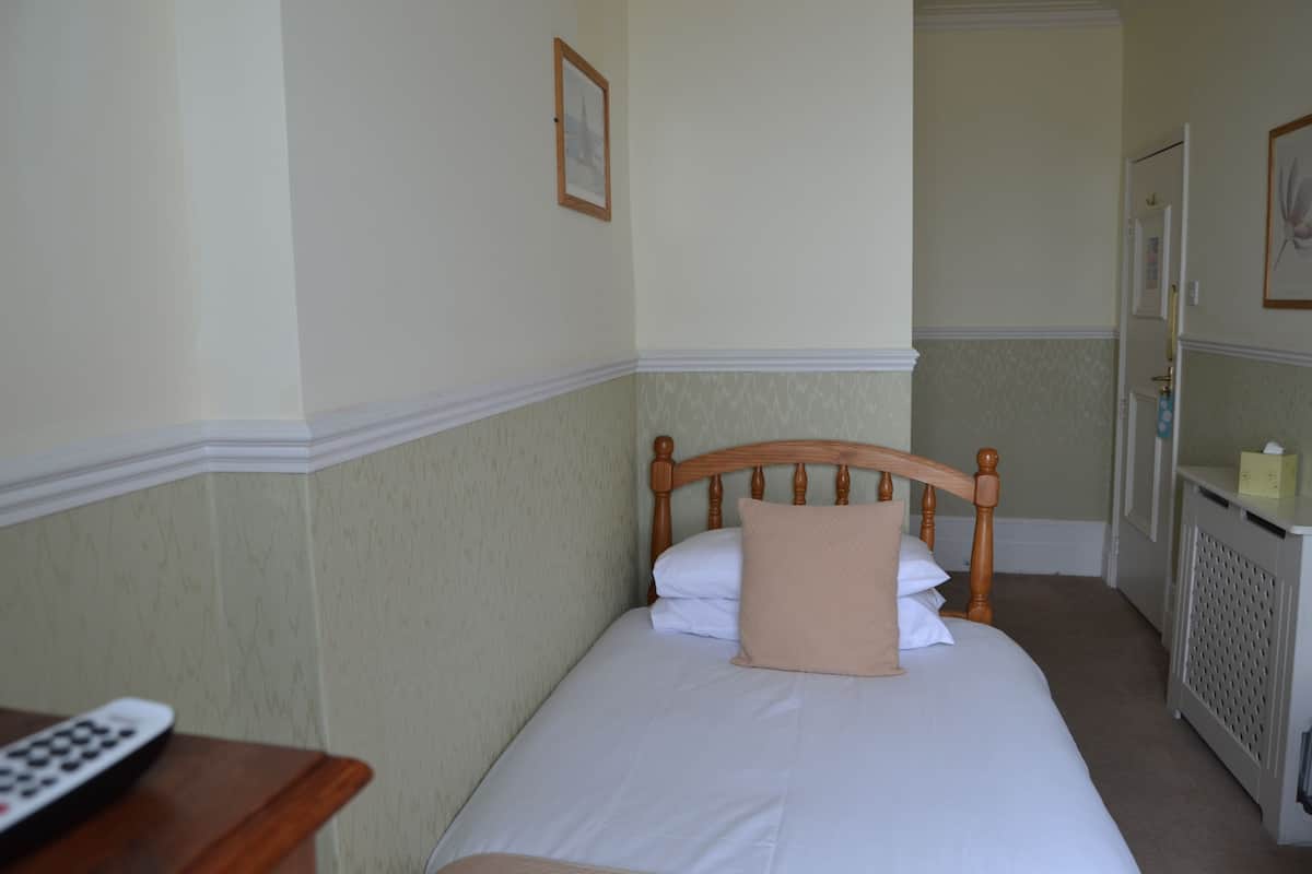 A neatly made bed with white and beige bedding, a wooden headboard, and a remote control on a wooden nightstand.