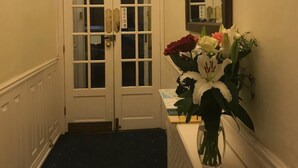 A hallway with double doors, a mirror, and a vase of flowers on a console table. - The Lindum (Hastings)