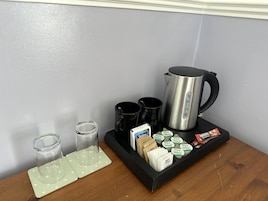 A coffee station with a kettle, cups, and sugar packets.